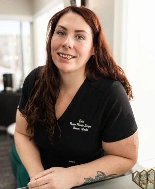 Woman with reddish-brown hair and a black scrub top, smiling and looking at the camera.